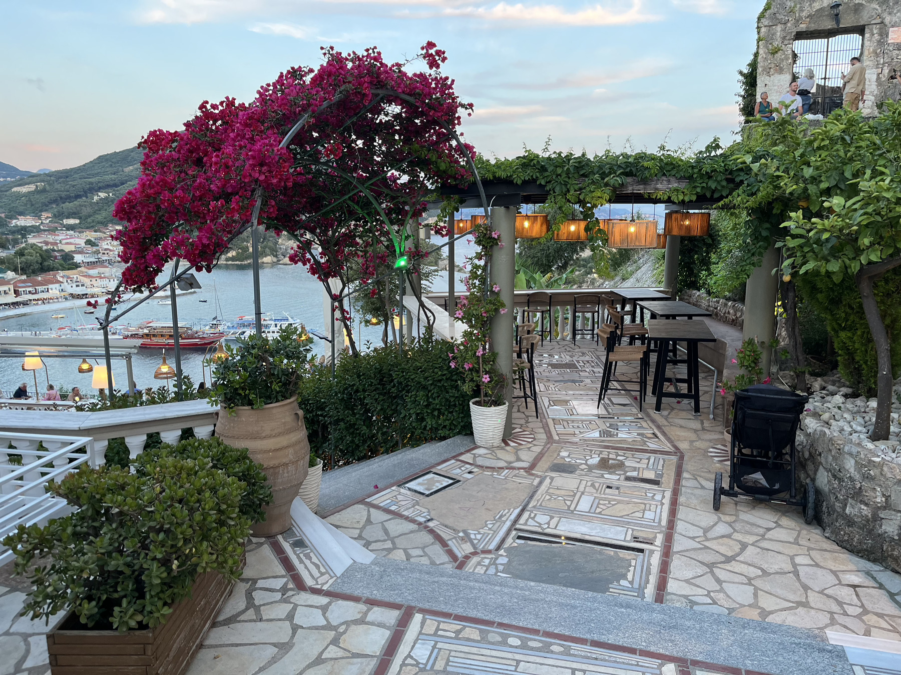 En pittoresk terrass med havsutsikt, prydd med blommande bougainvillea och omgivande grönska.